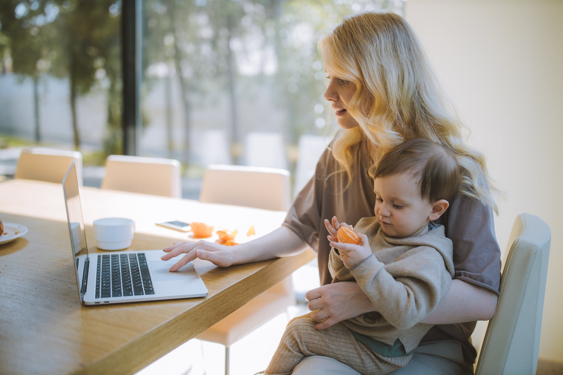 Young mother holding her young son on her lap while she types on a laptop.